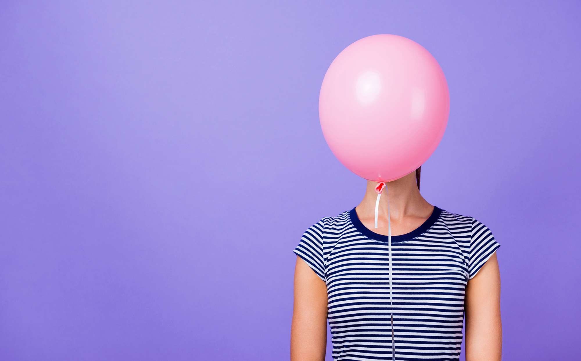 Kvinne foran lilla bakgrunn med rosa ballong som skjuler ansiktet.