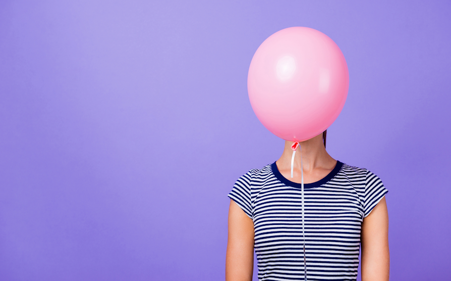 Kvinne foran lilla bakgrunn med rosa ballong som skjuler ansiktet.