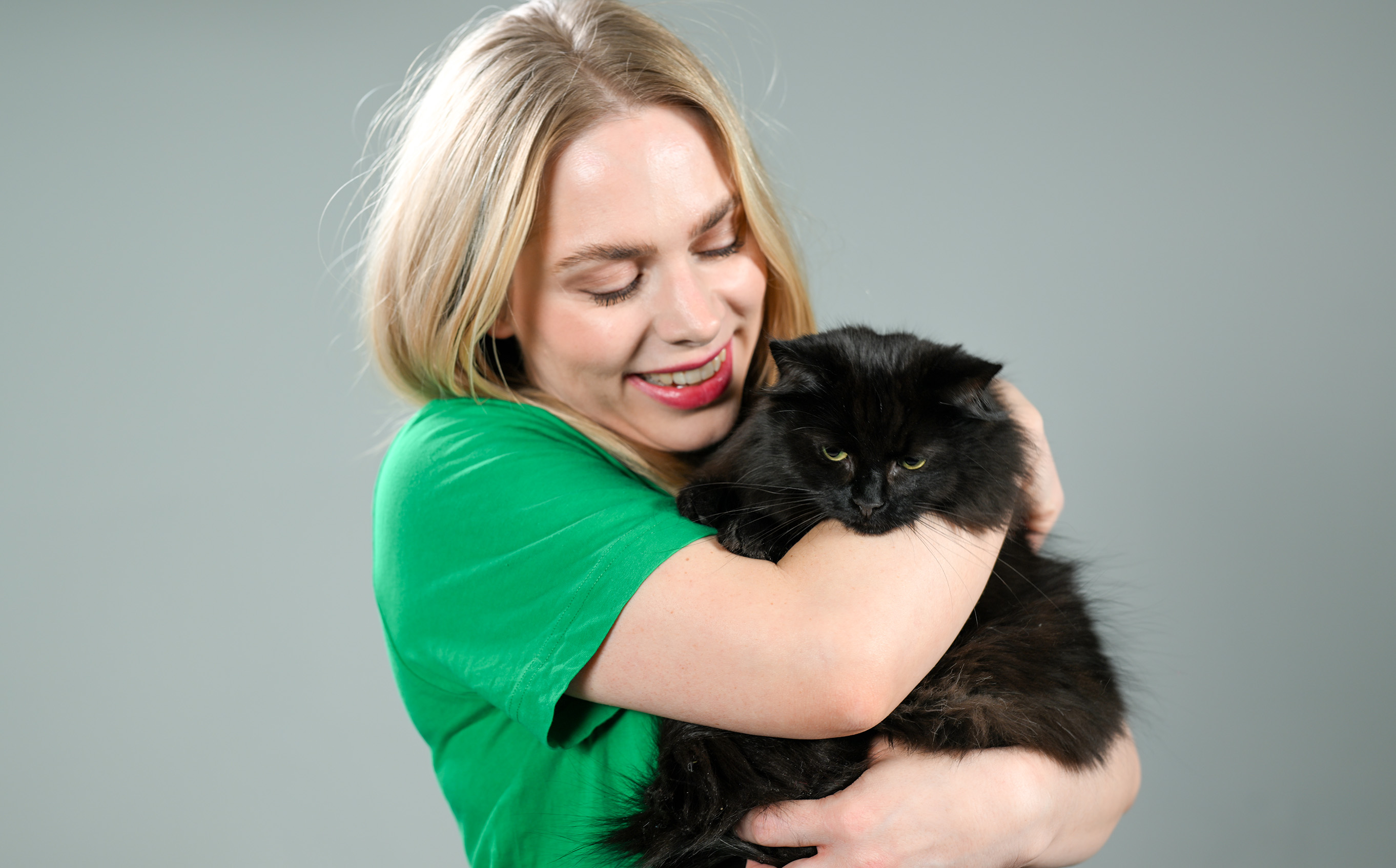 Kvinne i grønn t-skjorte som holder en svart langhåret katt