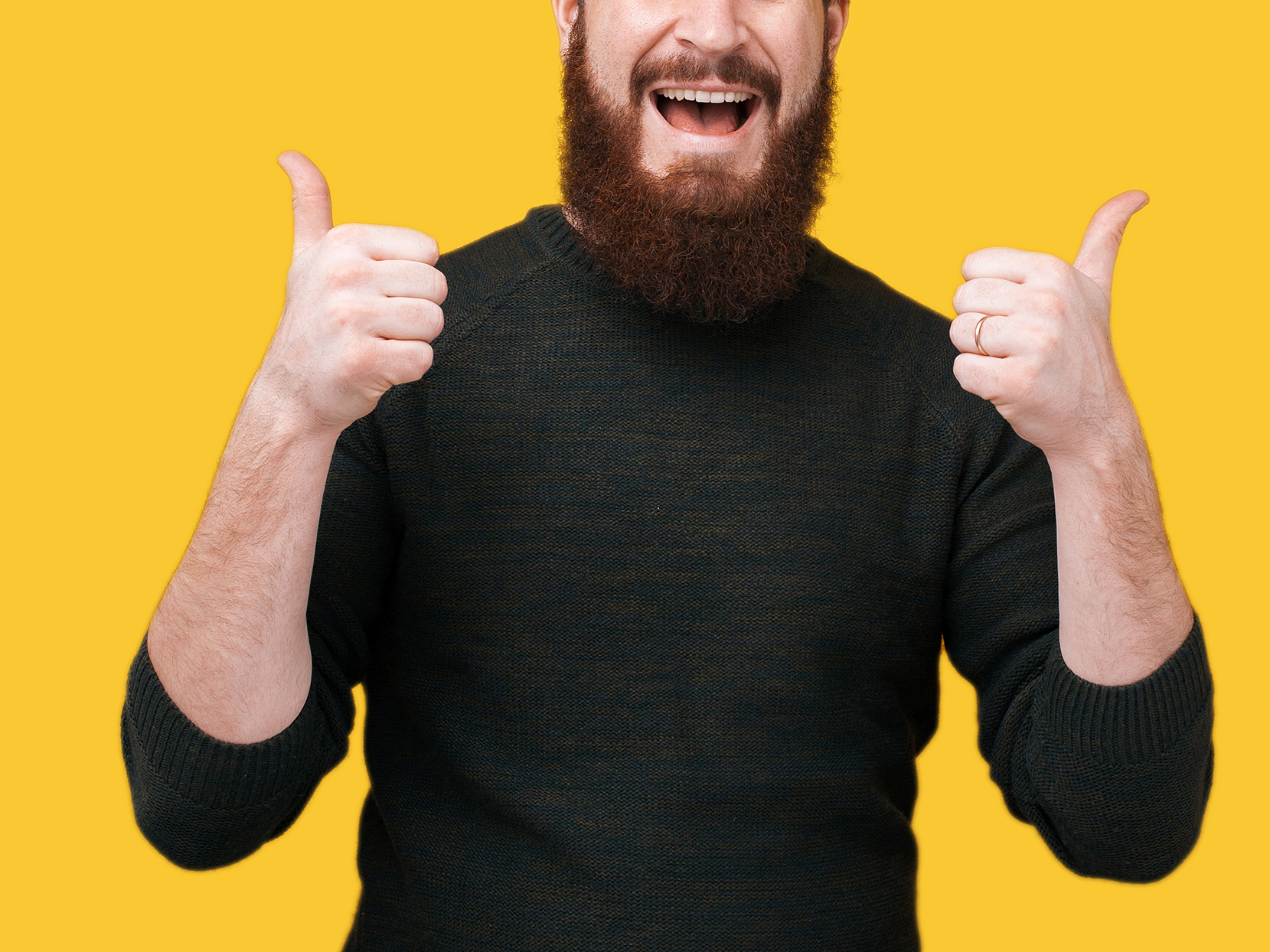 Utnsitt av halve hodet og overkroppen til en mann med brunt skjegg og grå genser som smiler og holder to tomler opp mot gul bakgrunn.