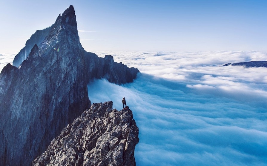 Illustrasjonsfoto av turgåer som står på toppen av Trollveggen og overskuer et tett, blått skylag