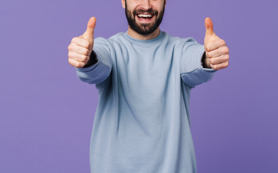 Mann i lyseblå genser viser to tomler opp foran lilla bakgrunn
