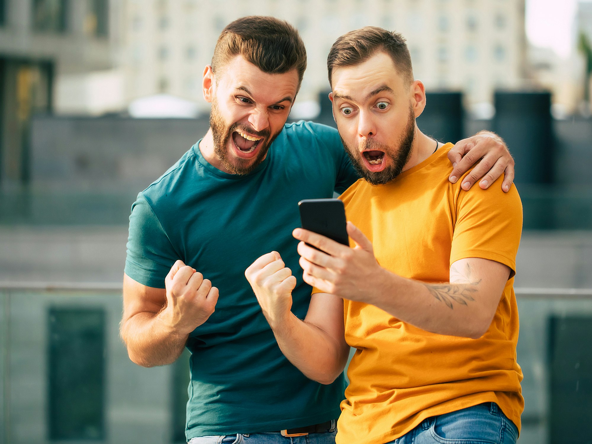 Illustrasjonsfoto av to menn med skjegg; den ene holder en mobil, den ene måper og den andre jubler over noe som foregår på skjermen