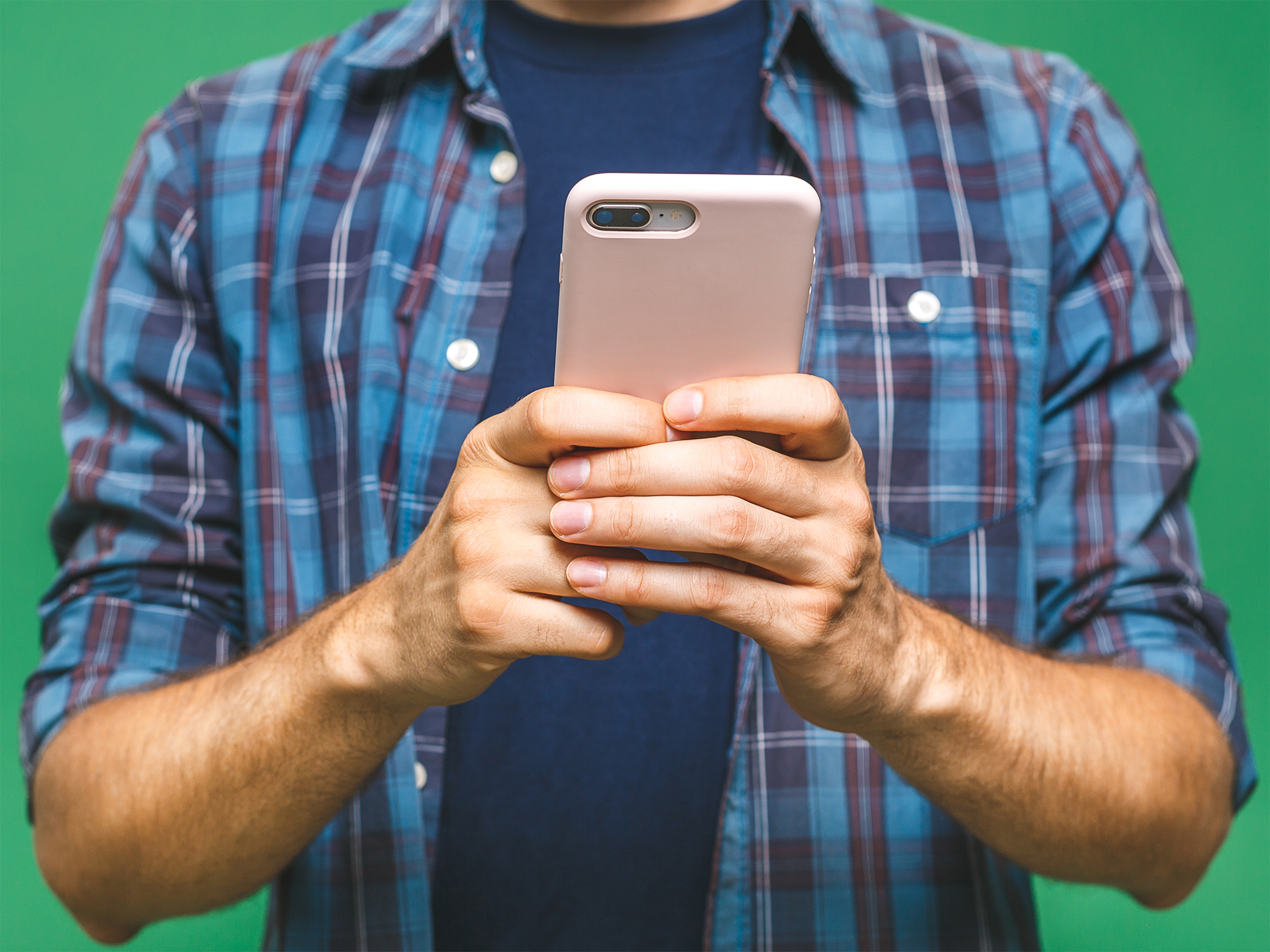 Illustrasjonfoto (beskjært) av mann i rutete skjorte som holder mobiltelefon, grønn bakgrunn
