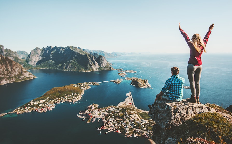 Mann og kvinne på toppen av et fjell med utsikt utover et tettsted og havet