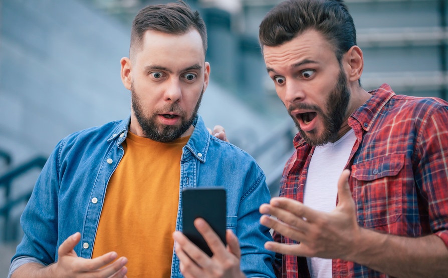 Illustrasjonsbilde av to menn. Ser på en mobiltelefon sammen, og er overrasket i uttrykket. Som om de har vunnet noe.