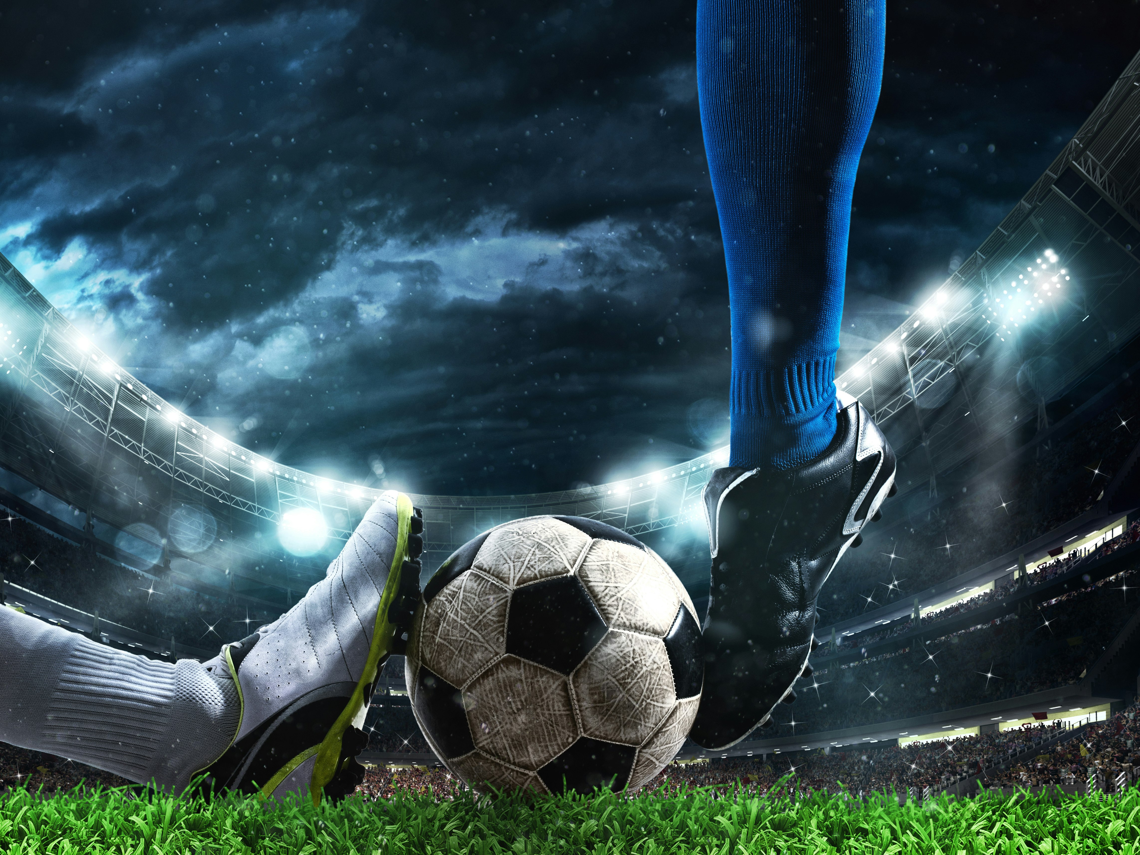 To fotballspillere kjemper om ballen. En med blå sko og en med svart sko