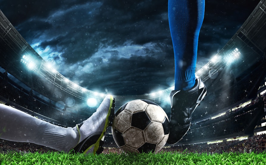 To fotballspillere kjemper om ballen. En med blå sko og en med svart sko