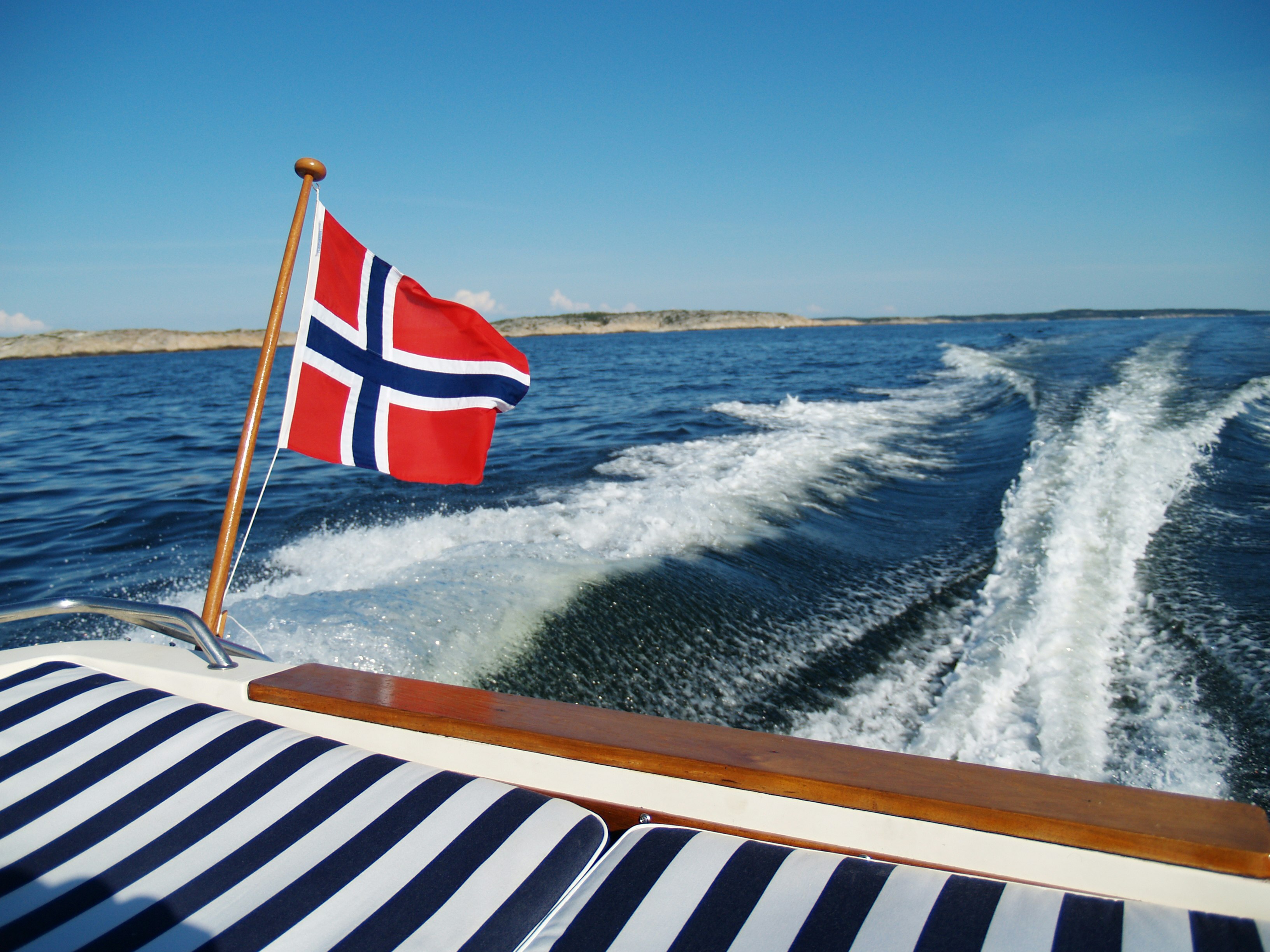 Bakenden av en privatbåt i fart på vannet med det norske flagget vaiende i vinden.
