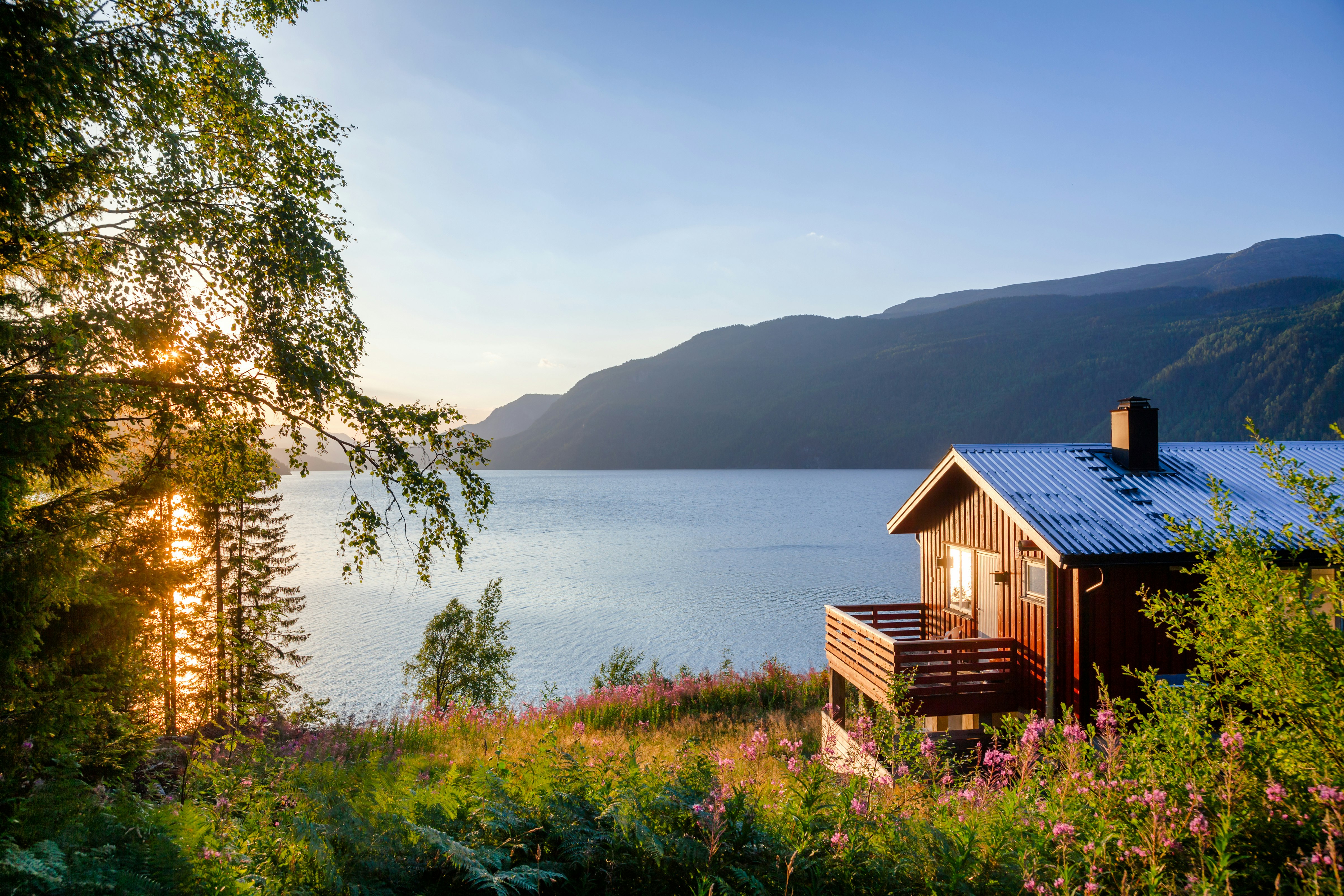 Utsikt over norsk sommerlandsskap med sjø og rødt feriehus.