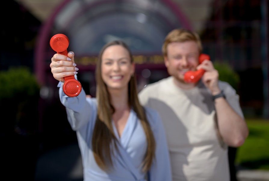 Ida Zachariassen og Lars Hulleberg med hver sin røde telefon utenfor Norsk Tipping