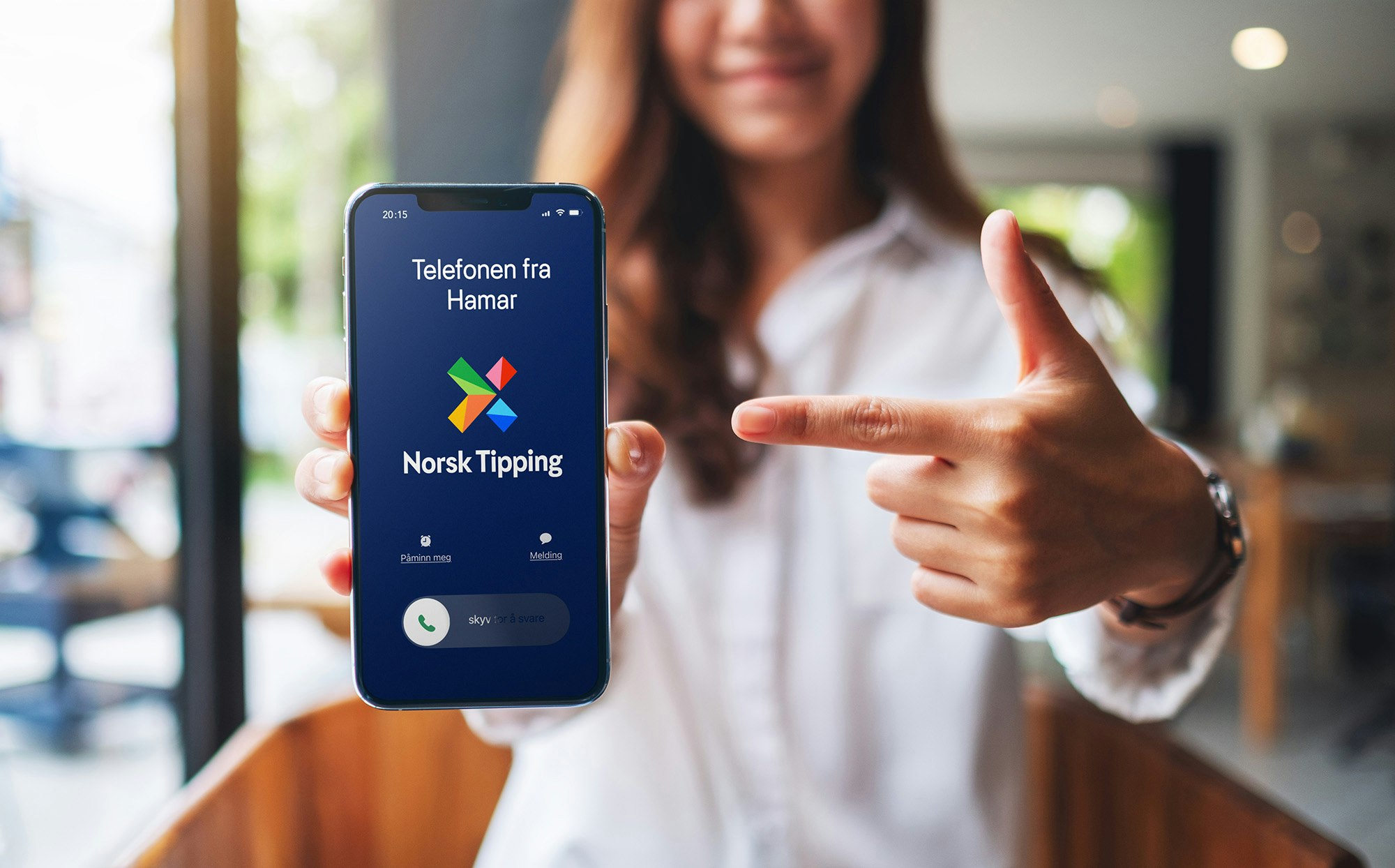 En kvinne som holder en telefon som viser et anrop fra Norsk Tipping - Telefonen fra Hamar