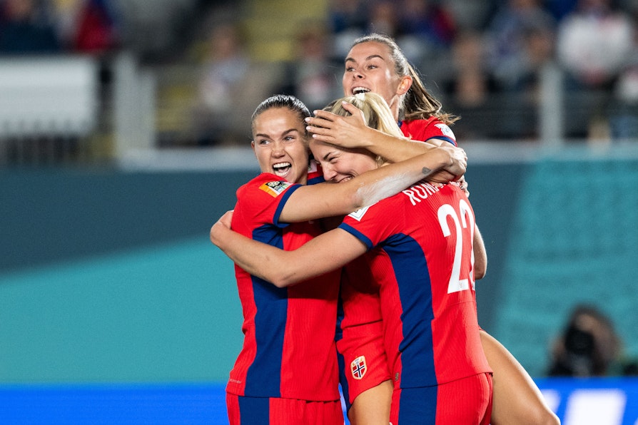 Tre kvinnelige fotballspillere jubler etter scoring. De har på seg røde drakter og røde shortser, Emilie Haavi, Sophie Roman Haug og Guro Reiten.