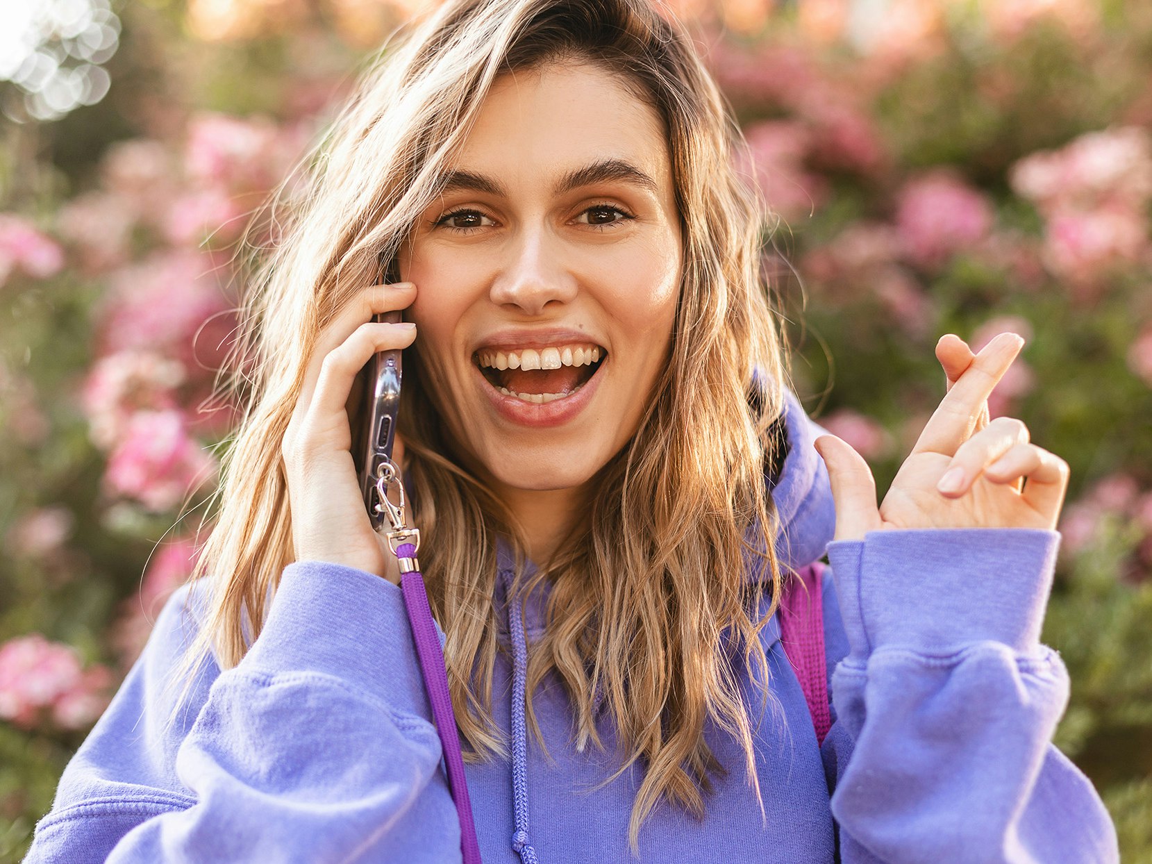 Kvinne med lille hoodie snakker i telefonen og krysser fingrene