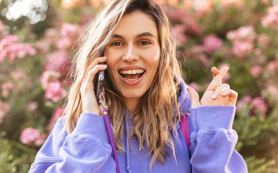 Kvinne med lille hoodie snakker i telefonen og krysser fingrene