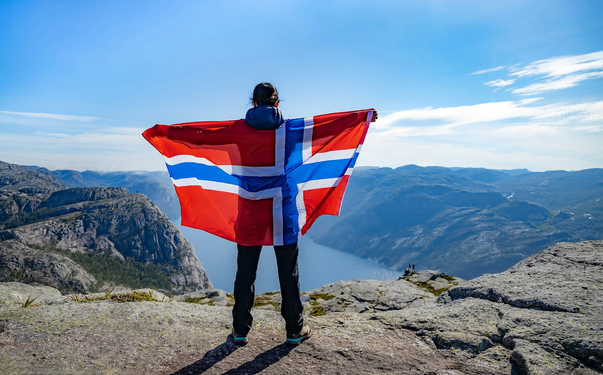 Kvinne som holder et norsk flagg på toppen av et fjell