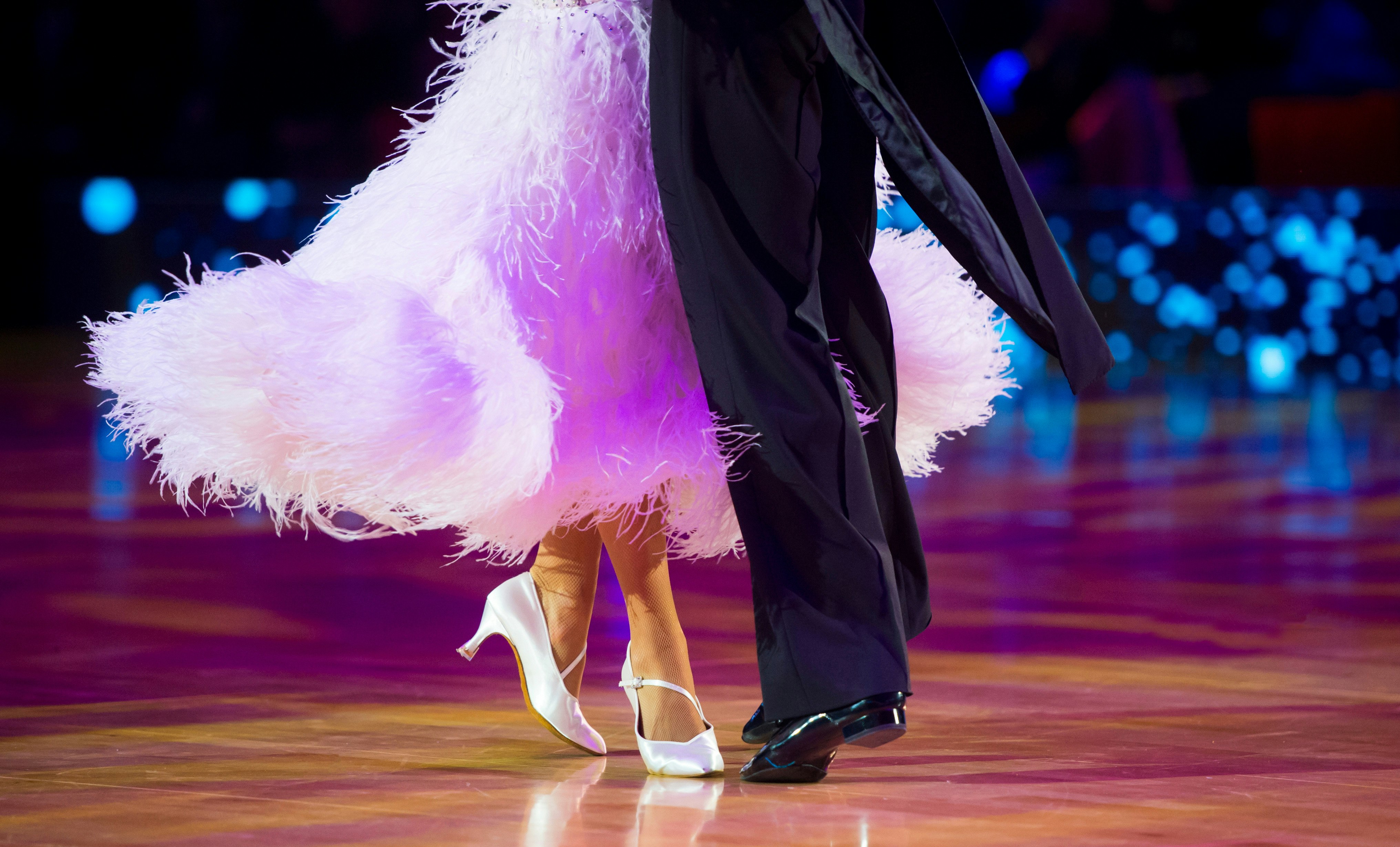 To som danser, ei dame i kjole og hvite pensko og en mann i svart dress