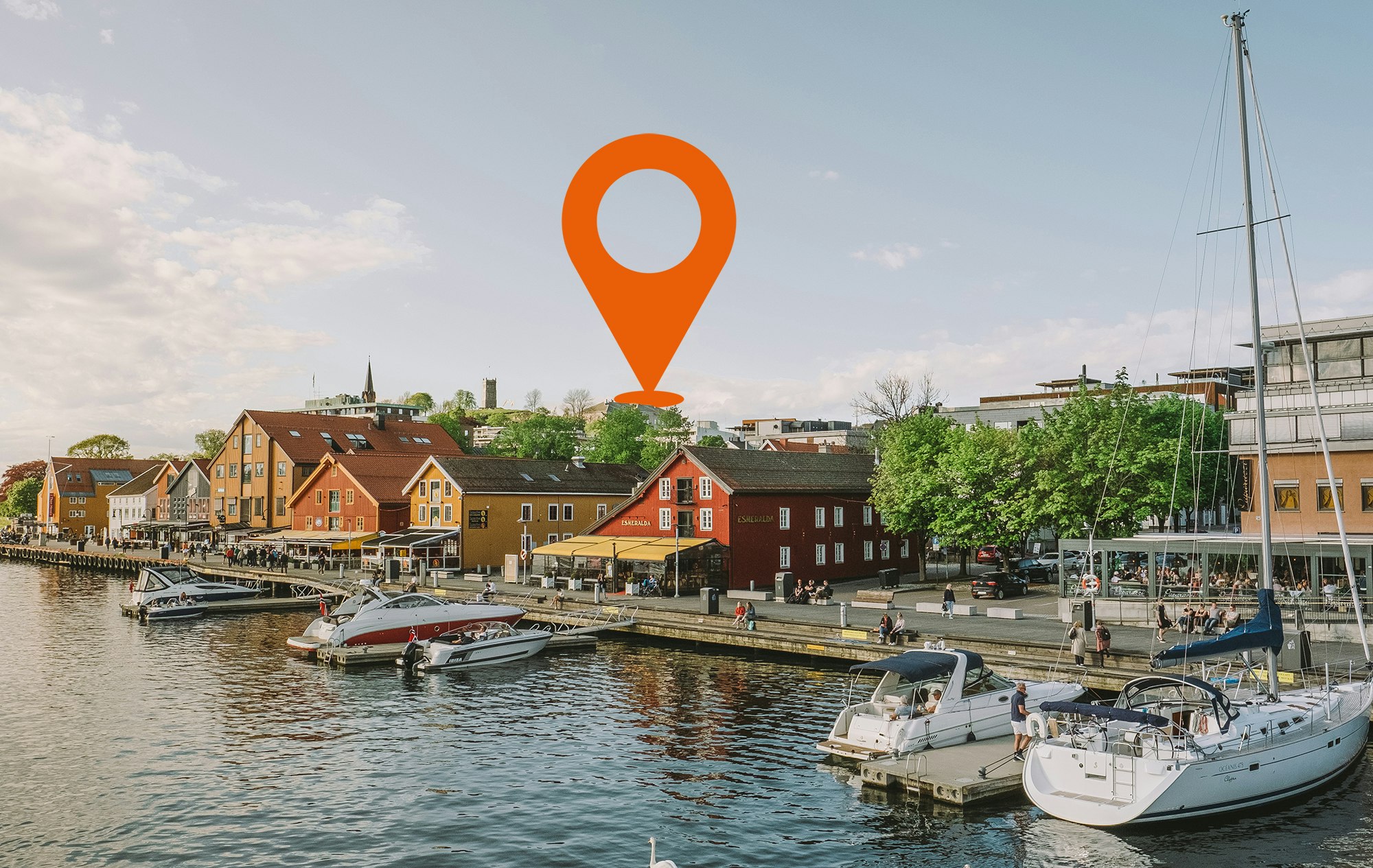 Bilde av bryggeområdet i Tønsberg sommerstid. Båter fortøyd, mennesker i gatene bak.