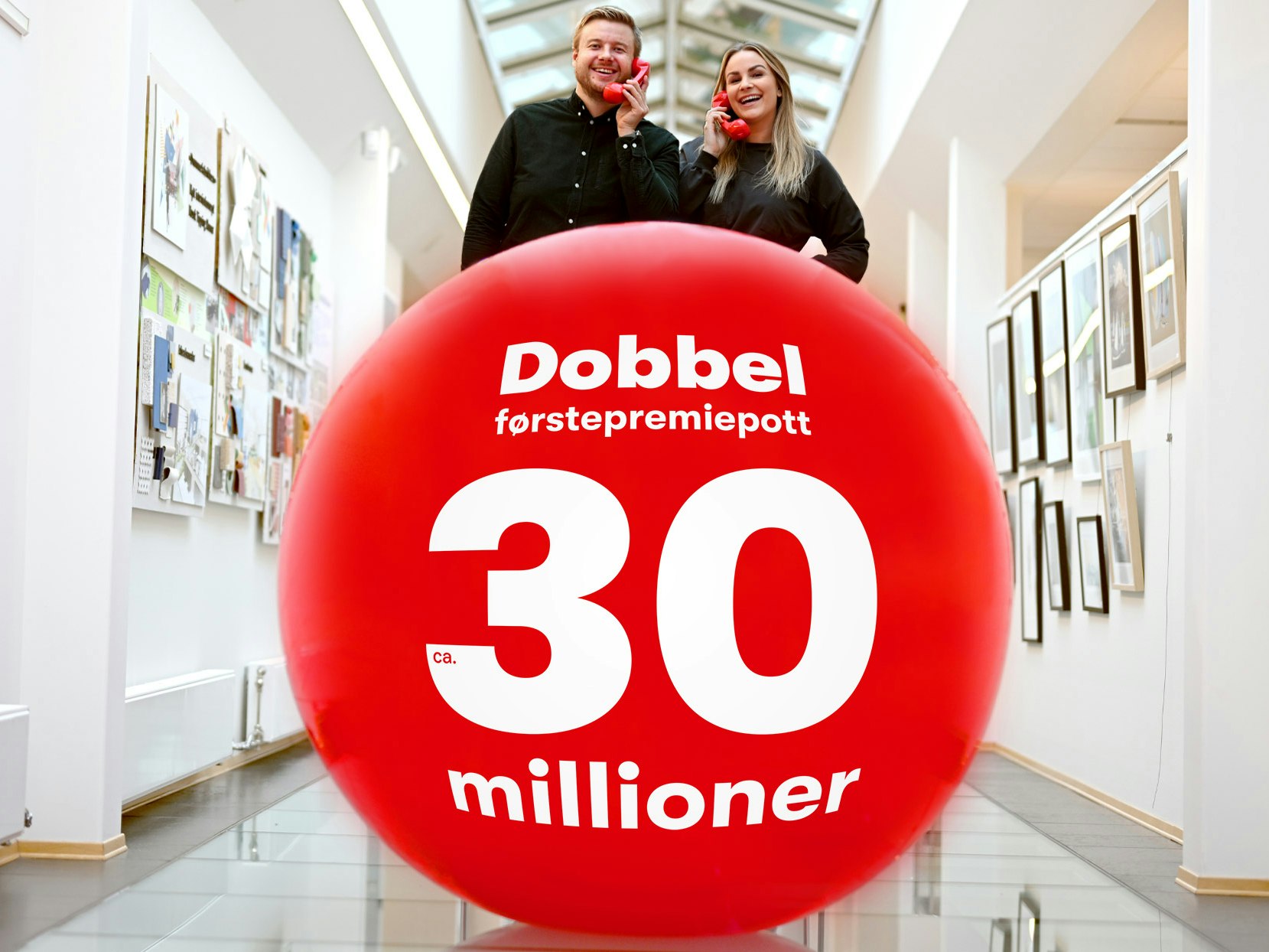 Trekningsredaktørene Lars Hulleberg og Pie Skagsoset Norseng står bak en stor rød ball med Lotto-tekst og holder hvert sitt røde telefonrør.