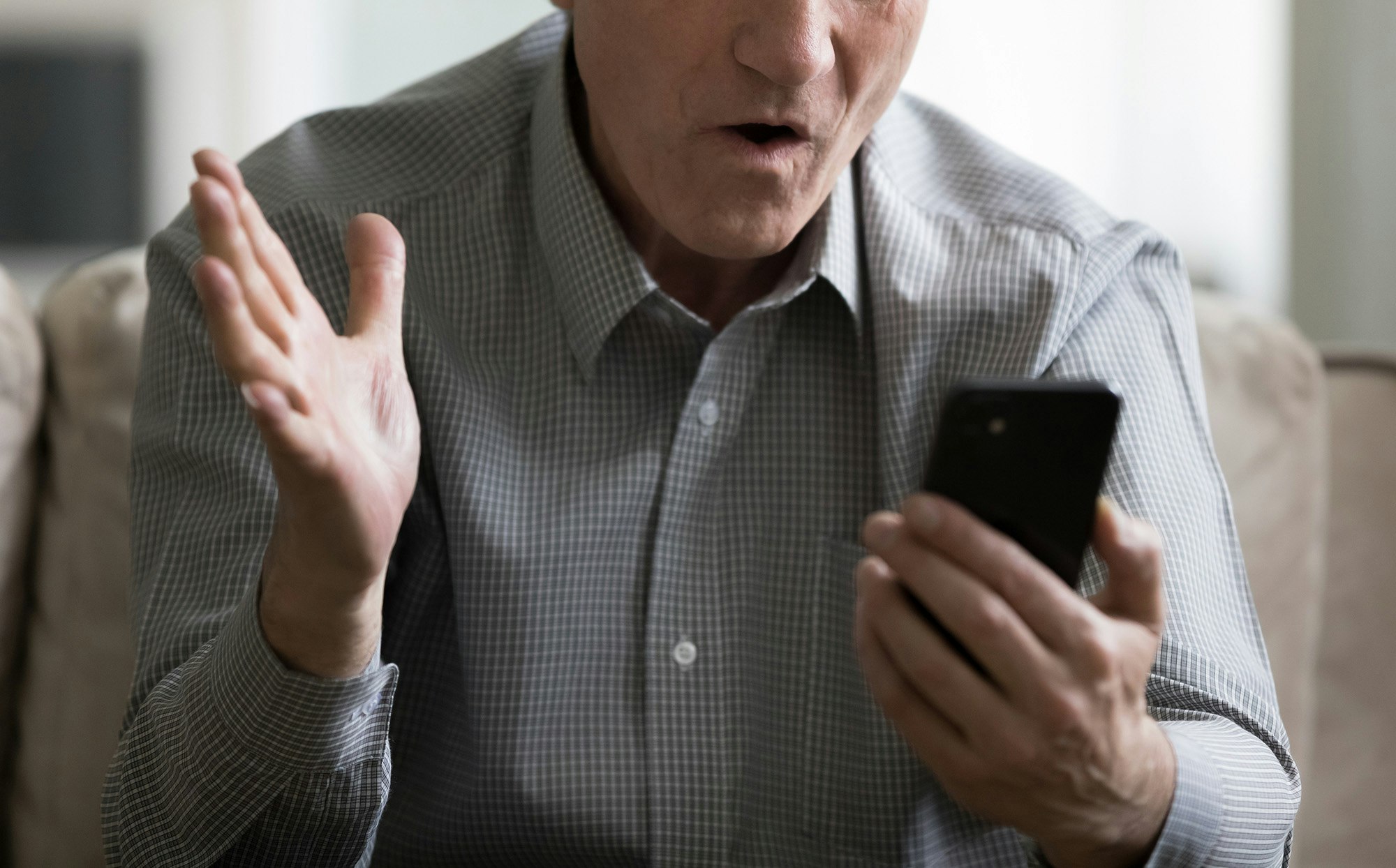 Mann holder en telefon å ser sjokkert på den