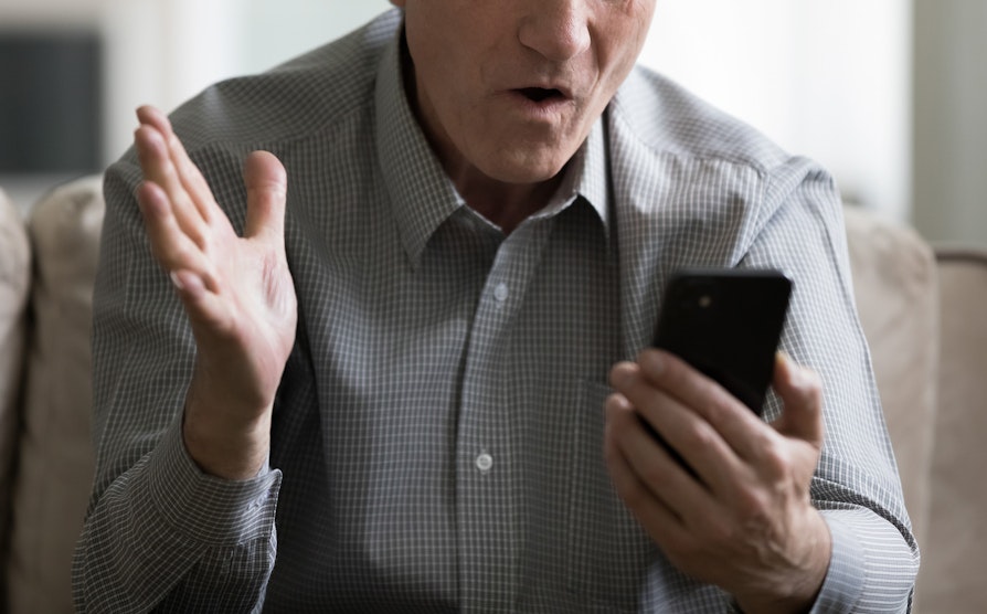 Mann holder en telefon å ser sjokkert på den
