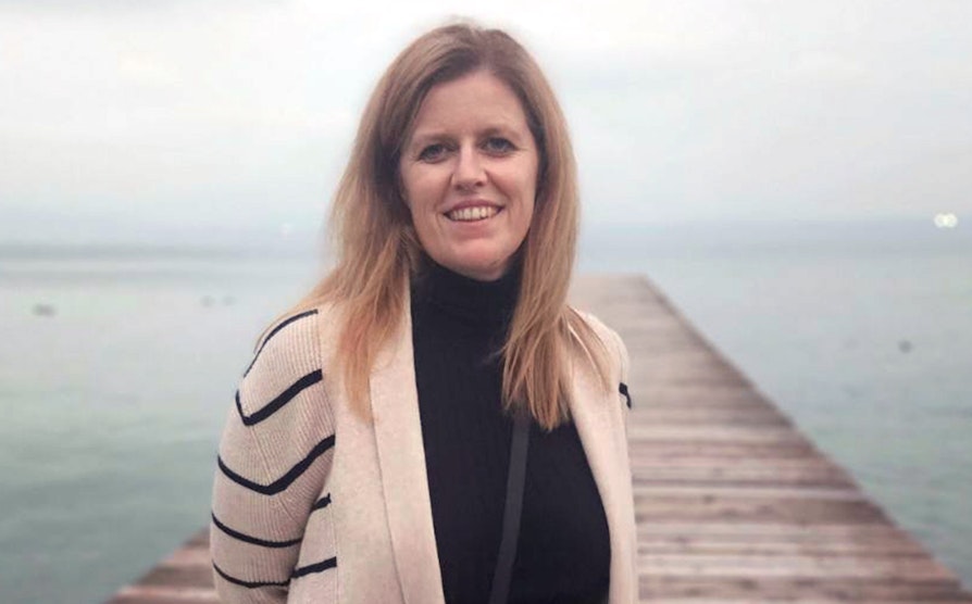 Portrett av Grete Pettersen Røddesnes iført sort høyalset genser og hvit- og sortstripete cardigan foran en trebygge ved en italiensk innsjø.