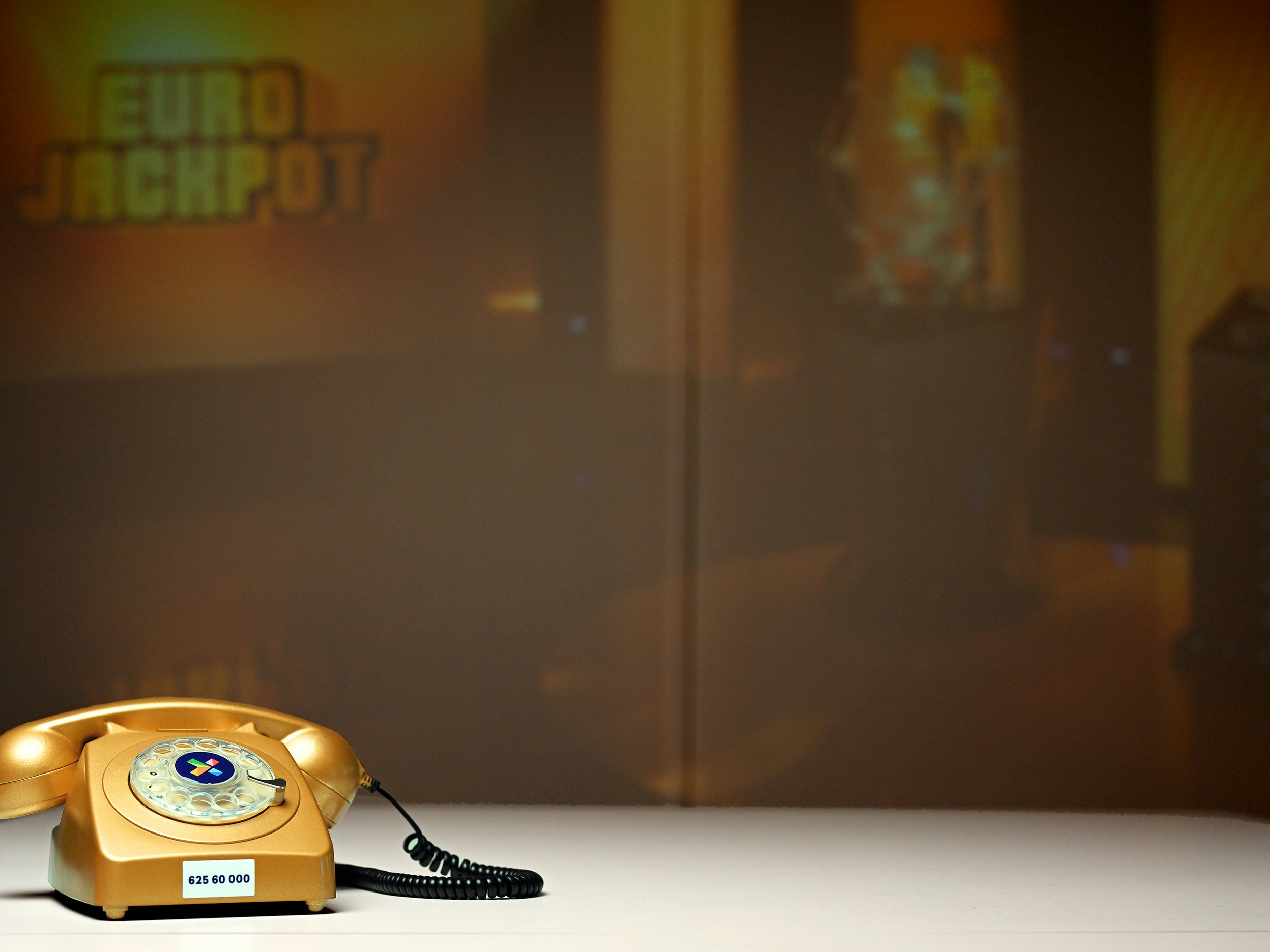 Bilde av "Telefonen fra Hamar" - i gullfarge. Eurojackpot-bilde i bakgrunnen.