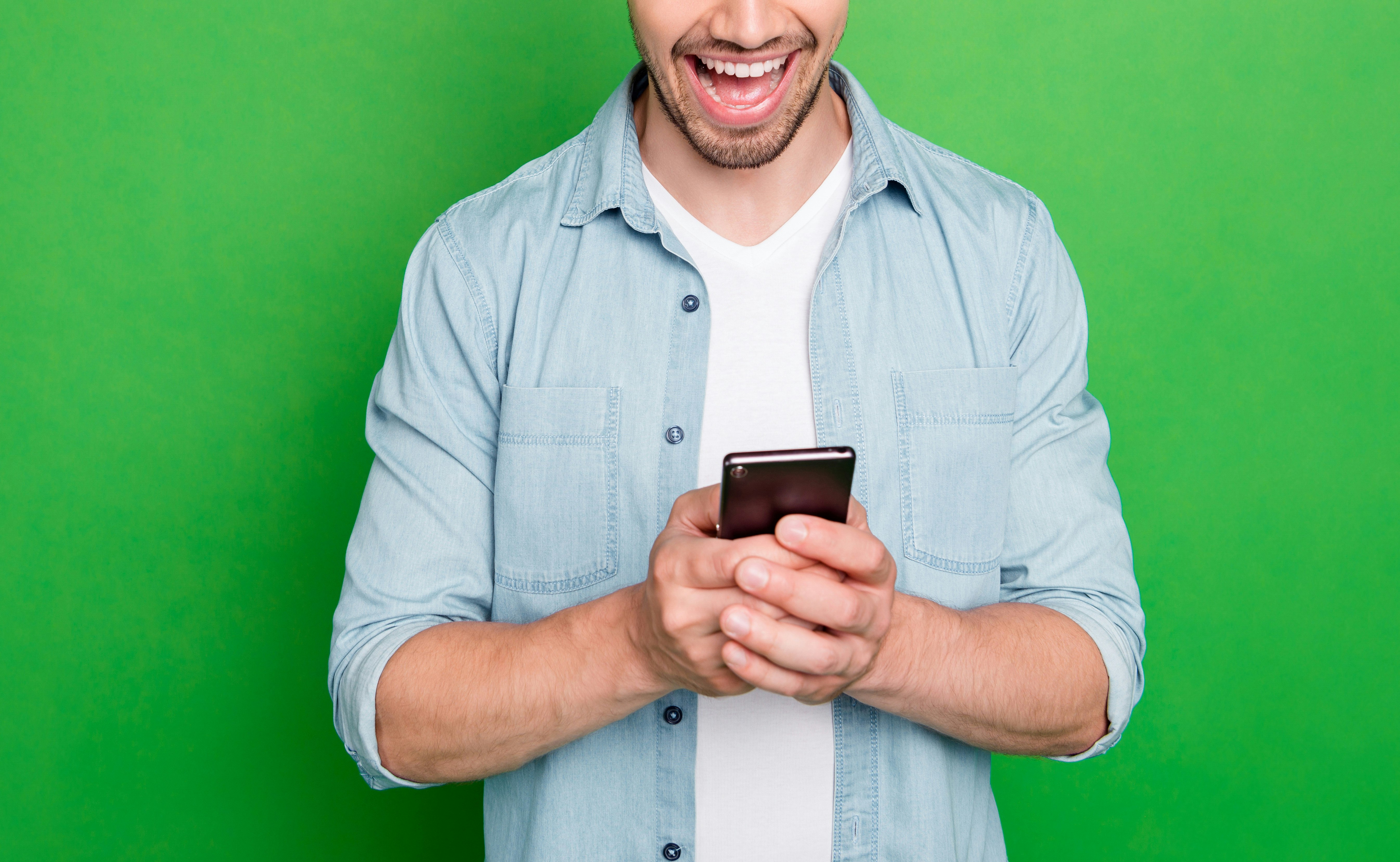 En mann i blå skjorte med mobil i hånden. Han smiler. Grønn bakgrunn.