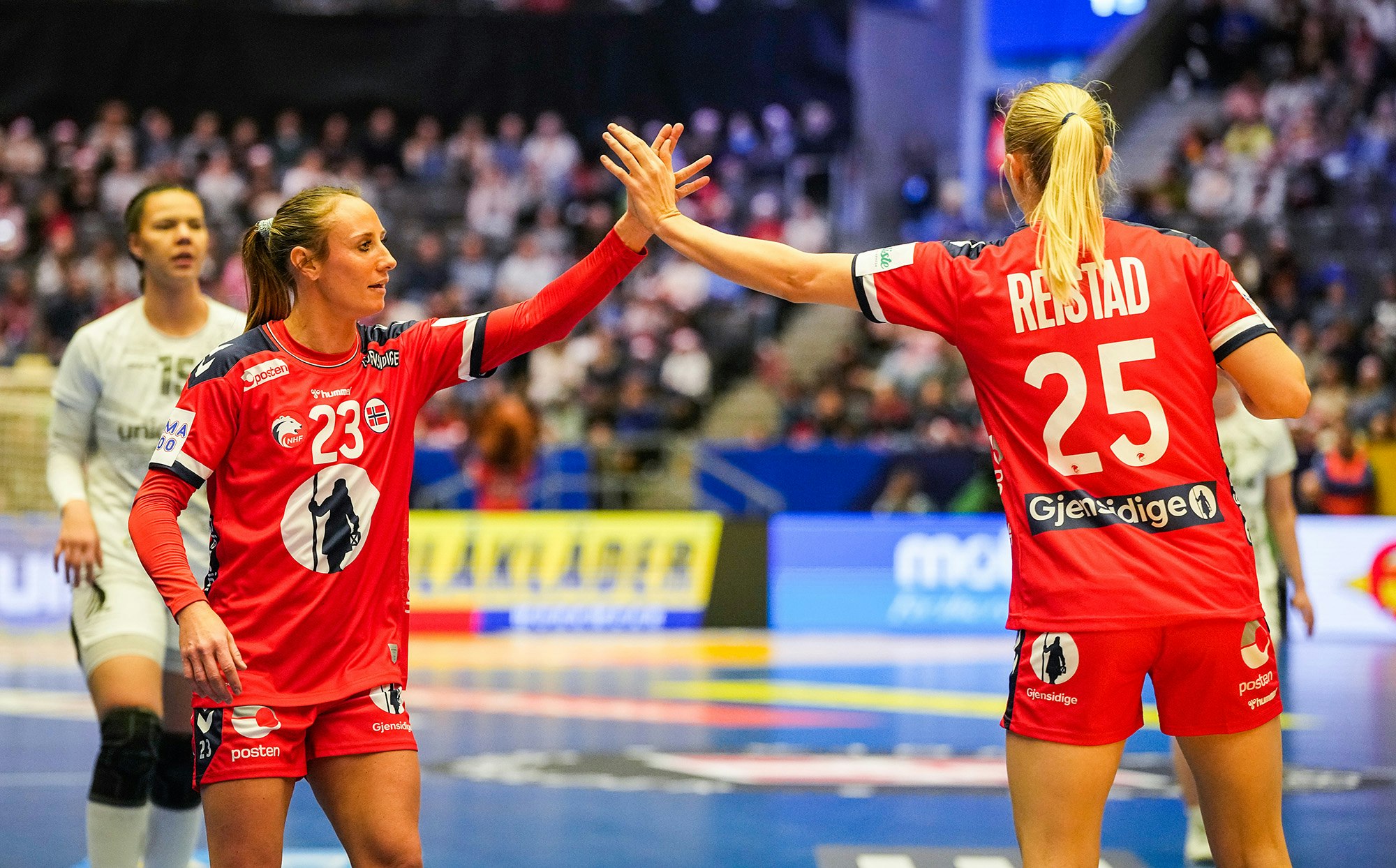 Bilde av to kvinnelige landslagsspillere i håndball som gjør "high five" på banen.
