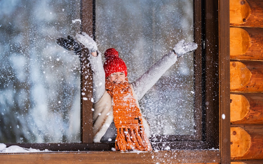Kvinne i hyttevindu som kaster snø mens hun smiler