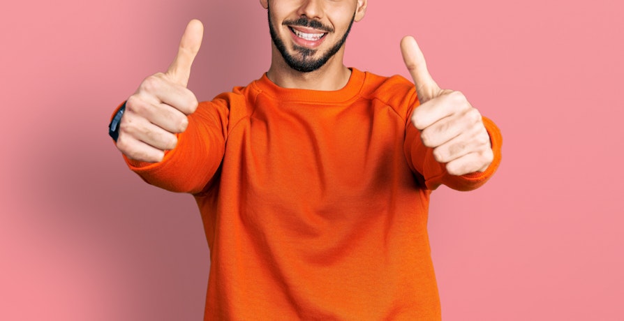 mann i oransje genser med tomlene opp
