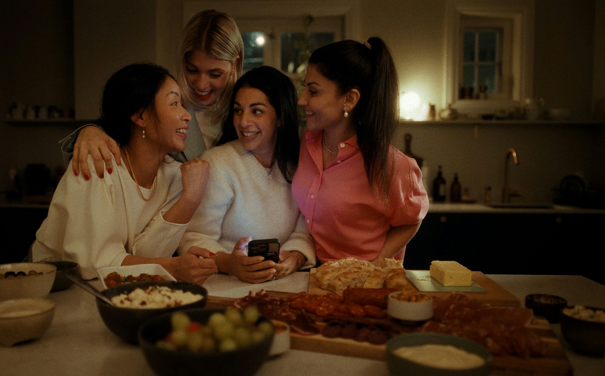 Fire unge kvinner som sitter sammen ved matbordet og oppretter spilledag på mobilen.