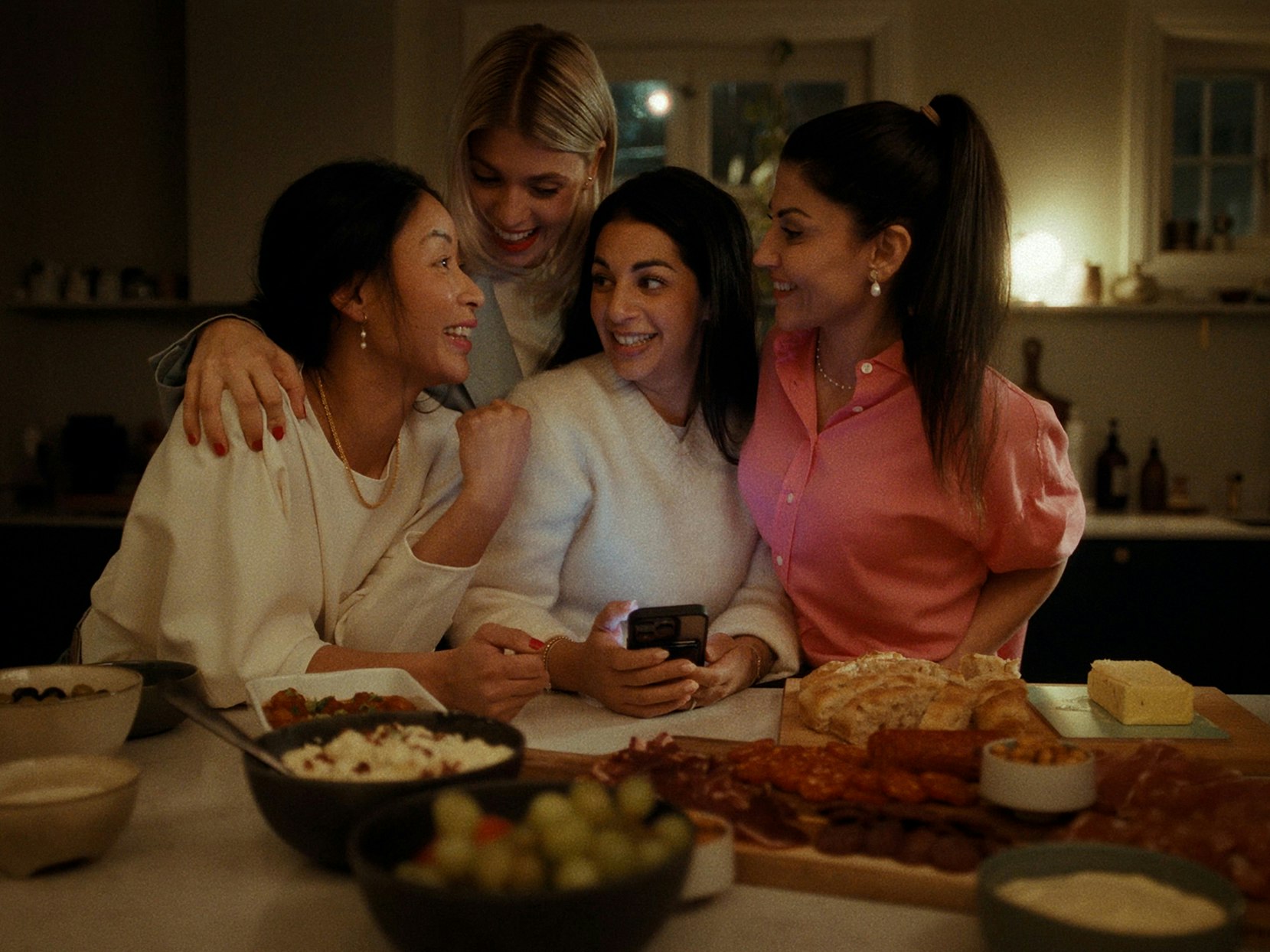 Fire unge kvinner som sitter sammen ved matbordet og oppretter spilledag på mobilen.