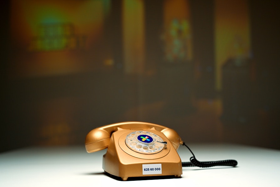 Bilde av gammeldags telefon i gullfarge. Står på et bord. Bak et lerret med Eurojackpot-logo.