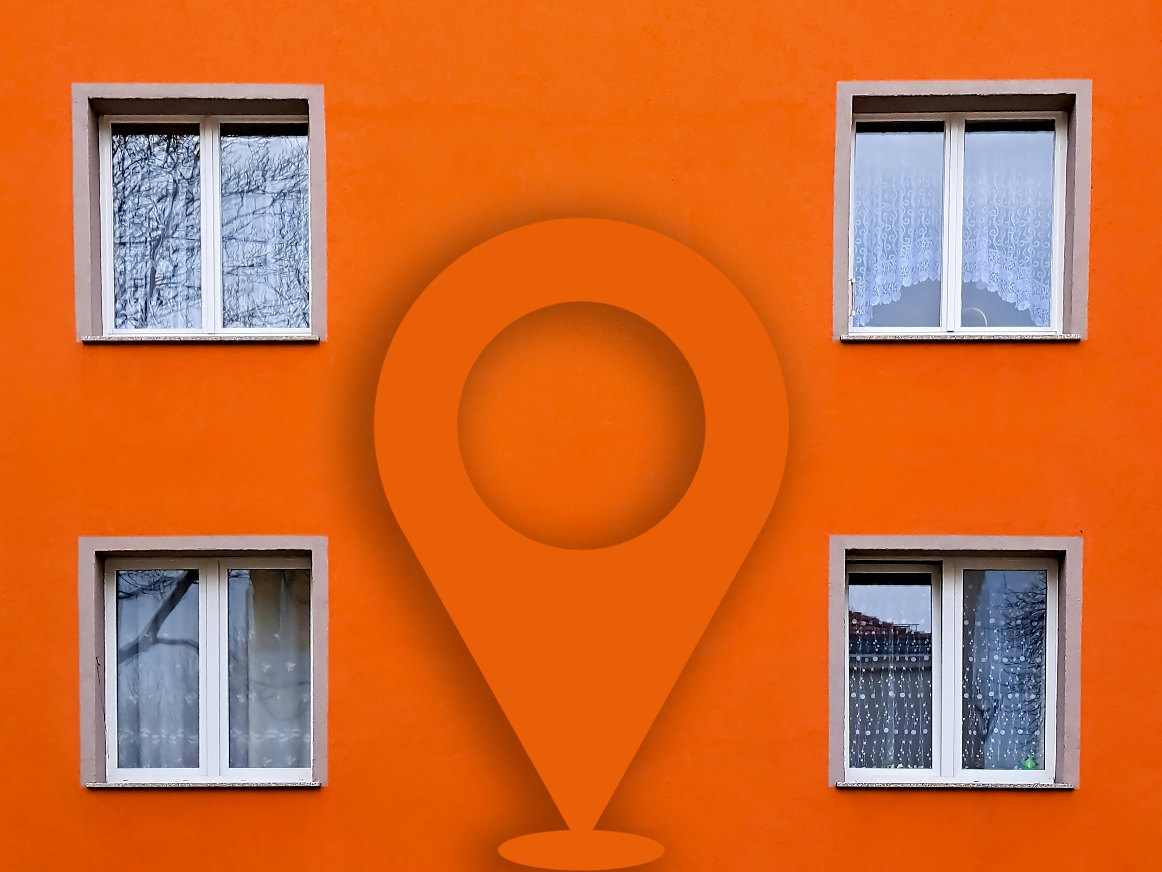 Bilde av en boligblokk. Bilde tatt tett på. Viser fire vinduer over to etasjer. Oransje farge. I midten av bildet er geotagen kjent fra Nabolaget limt inn.
