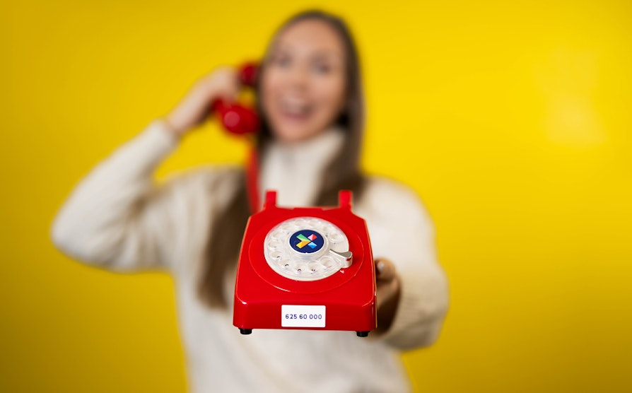 Kvinne holder i rød telefon med Norsk Tippings vinnernummer på. Supertrekning påske 2024.