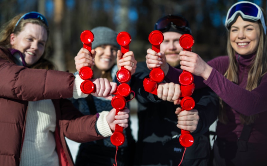 Fire personer i vårsola. Lager tallet 44 med røde telefoner. Supertrekning påsken 2024.