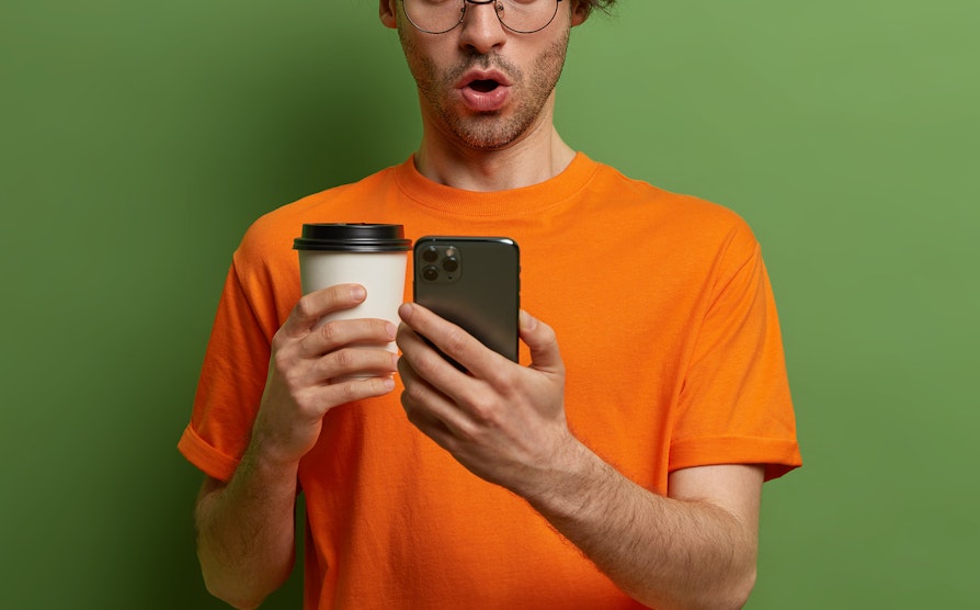 Mann ser overrasket ned på telefonen. Grøn bakgrunn. Flax