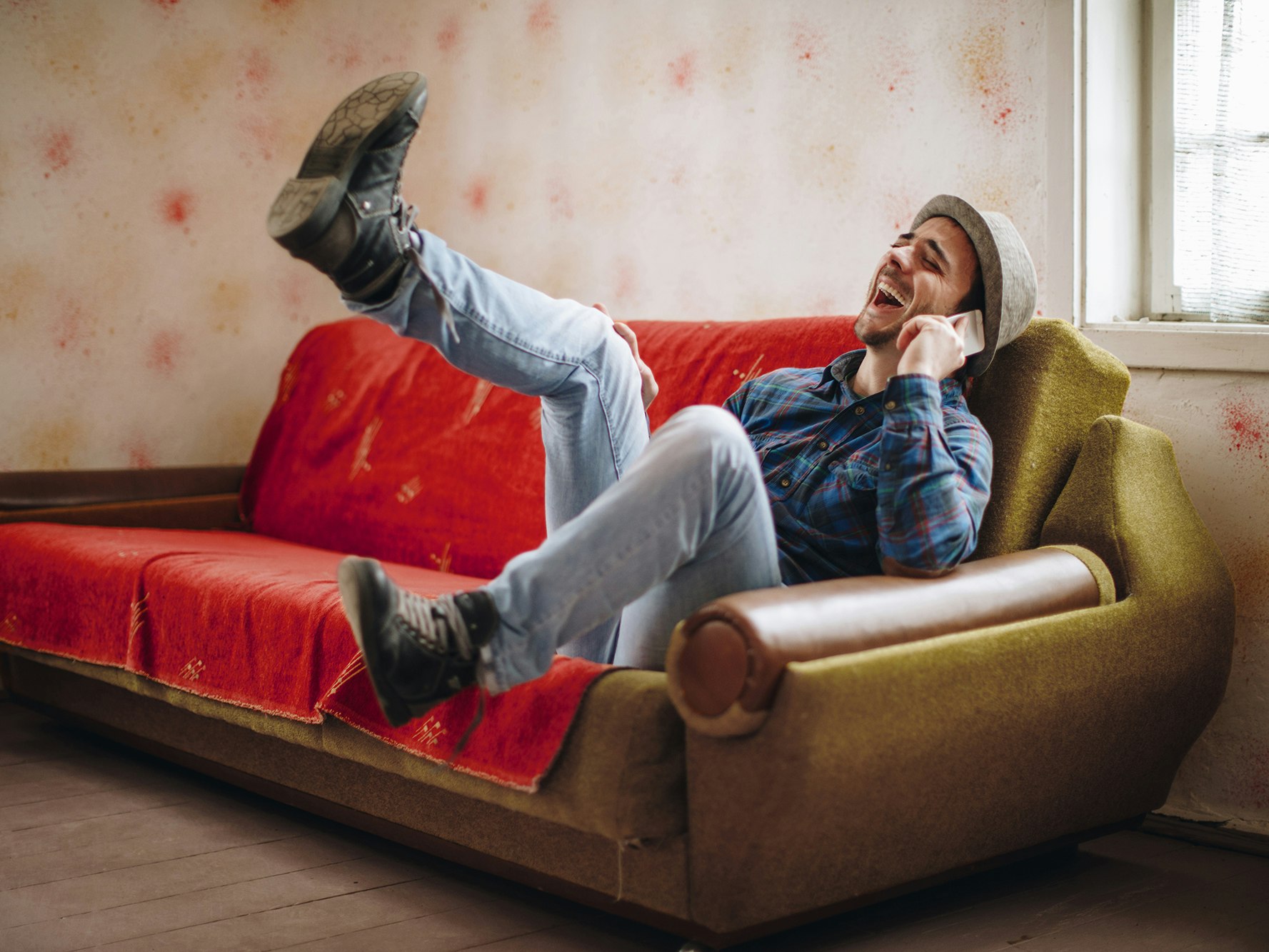 Bilde av en ung mann som sitter i en sofa. Prater i telefonen, og får tydeligvis en god beskjed. Kanskje sju rette i Lotto?