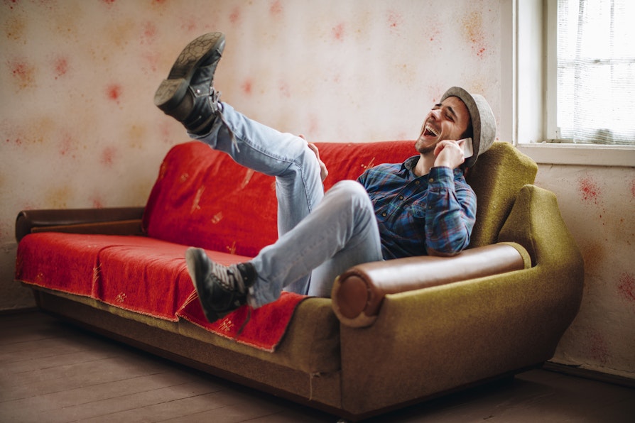 Bilde av en ung mann som sitter i en sofa. Prater i telefonen, og får tydeligvis en god beskjed. Kanskje sju rette i Lotto?