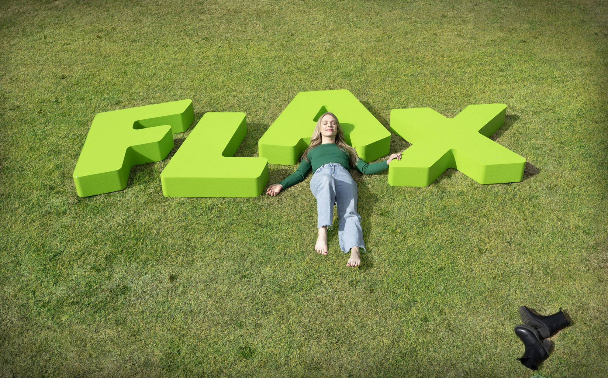 Kvinne ligger i gresset med og på bokstavene FLAX.