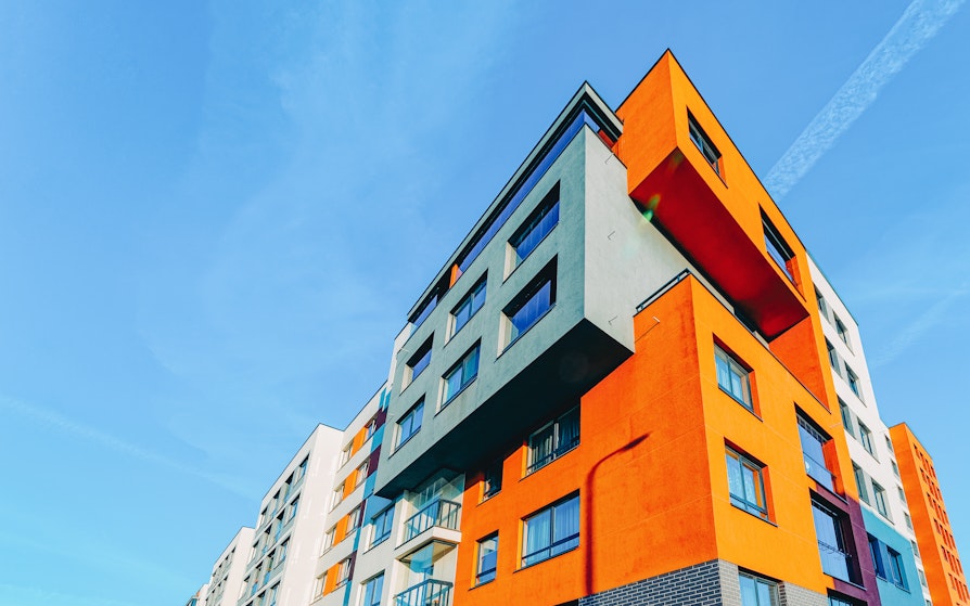 Undervinklet bilde av moderne boligblokk i hvite, grå, lilla og oransje farger mot blå himmel.