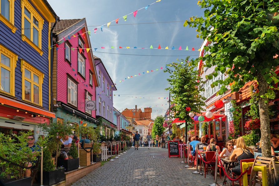 Gågate med fargerike bygninger og mennesker som sitter på uteserveringer i Stavanger om sommeren.