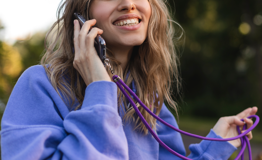 Halvsnitt av kvinne med blondt langt hår og lilla genser som smiler og holder en mobiltelefon opp mot øret.