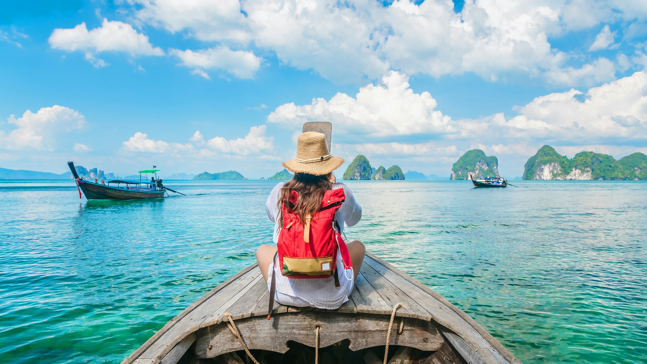 Bilde av kvinne på en båt ute på vannet i Thailand. Ryggen til. Rød ryggsekk. Noen båter rundt.