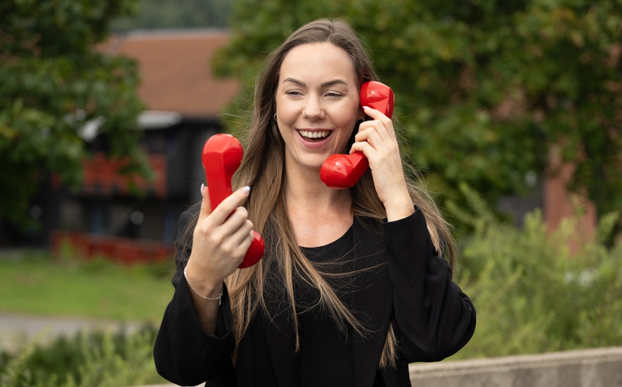 Bilde av en kvinne som holder ti to røde telefoner, ute i høstlige farger.