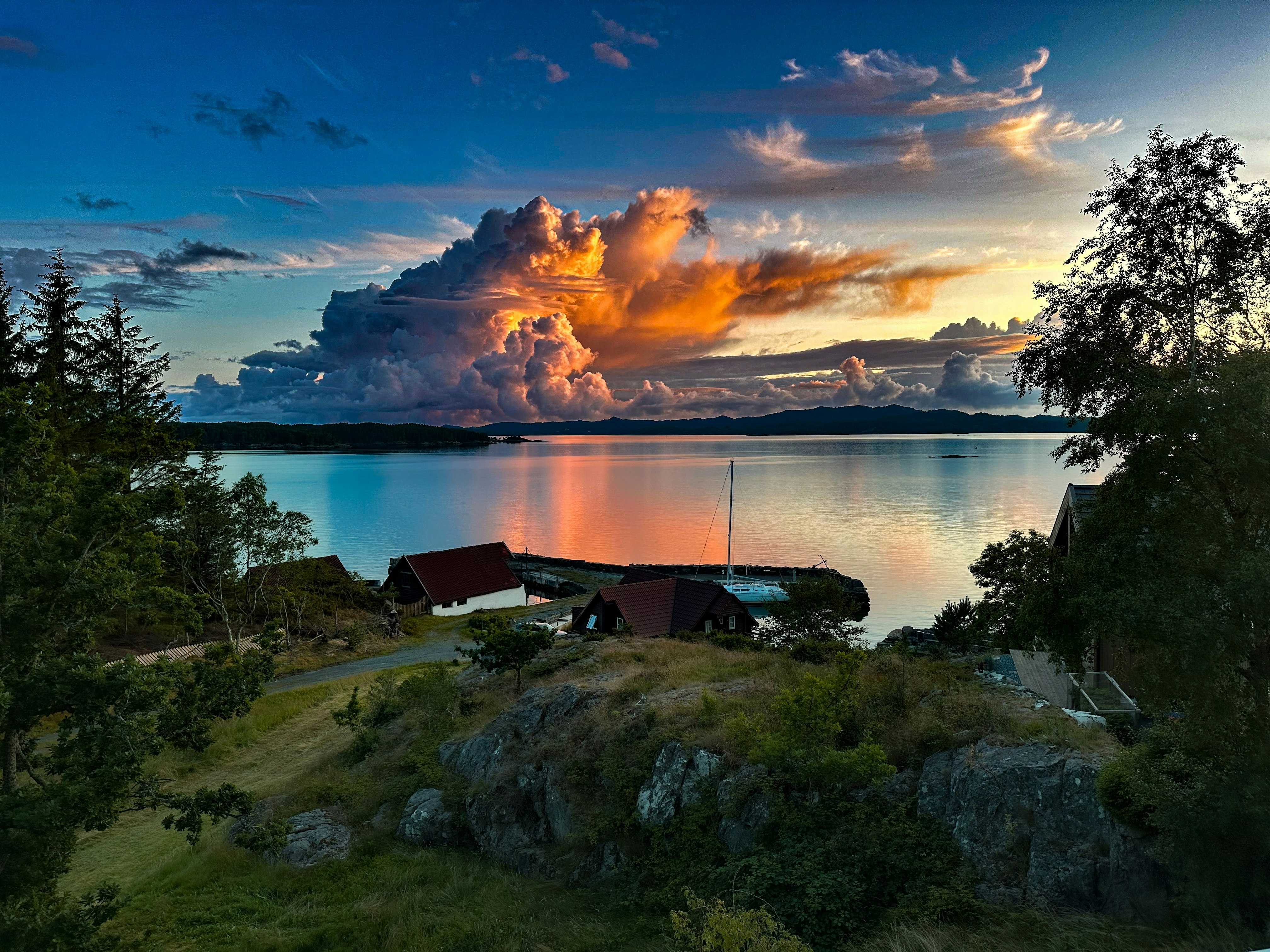 Utsikt mot fjorden og hus i Bømlo sommerkveld, med oransje skyer på himmelen