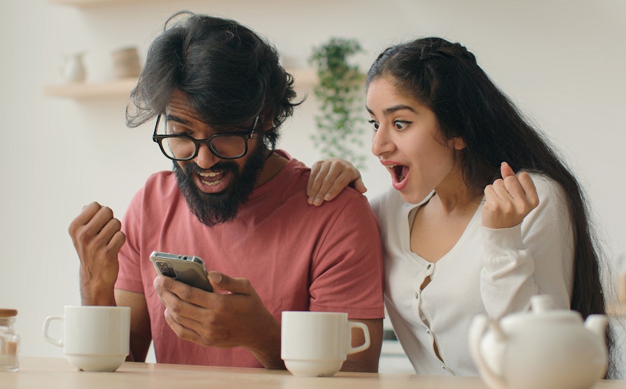 Overrasket og glad mann og dame ser sammen på telefon.