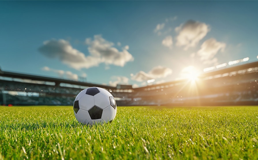 En fotball på gresset på en solfylt fotballstadion.
