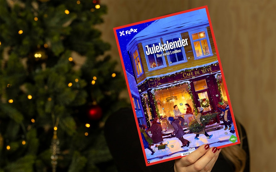 Kvinnehånd med røde negler holder opp en Flax Julekalender med et juletre ute av fokus i bakgrunnen.